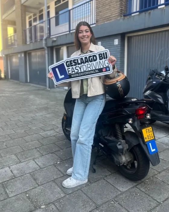 Geslaagde scooterleerling met het bord Geslaagd bij Easydriving naast een zwarte scooter