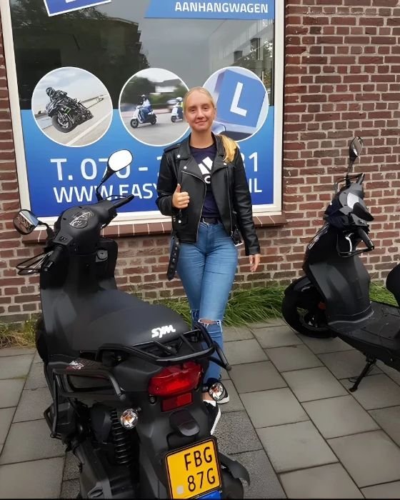 Geslaagde scooterleerling tussen twee zwarte scooters, voor een raam met rijschoolreclame