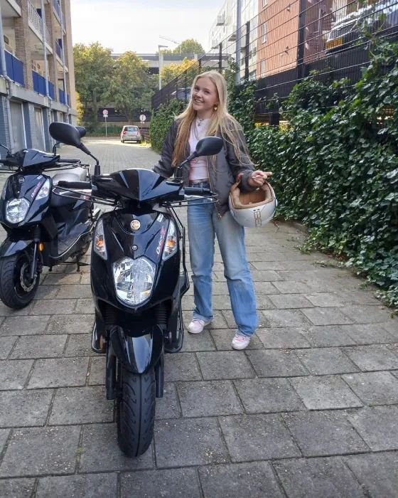 Geslaagde scooterleerling naast twee zwarte scooters in een straat