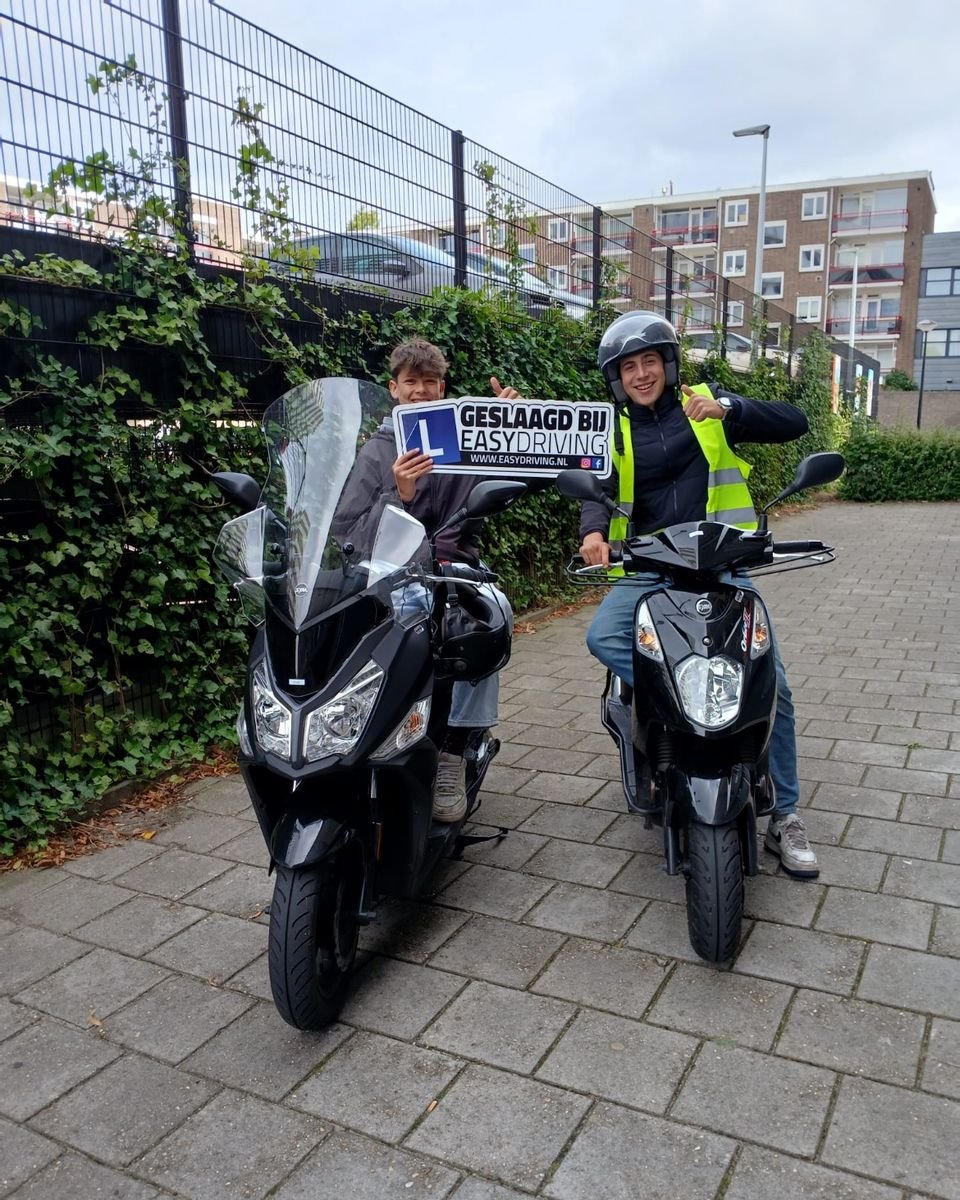 Twee geslaagde scooterleerlingen op twee scooters, een van hen houdt het bord Geslaagd bij Easydriving omhoog